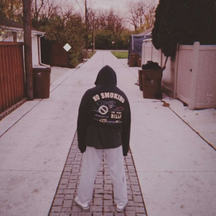 MAUD customer in a No Smoking in the Hills back print hoodie, standing in an alley